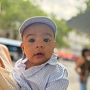 Antoine participe au concours pour gagner de l'argent avec cette photo : baby, child, infant, face, hat, cap, shirt, striped_shirt, person, outdoor, urban, blurred_background, curious, portrait, close_up, holding, adult, daylight, expression, cute