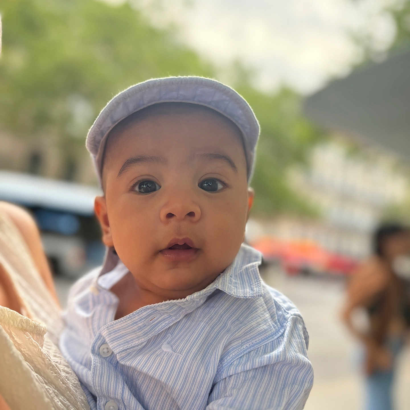 Antoine participe au concours pour gagner de l'argent avec cette photo : adult, baby, blurred_background, cap, child, close_up, curious, cute, daylight, expression, face, hat, holding, infant, outdoor, person, portrait, shirt, striped_shirt, urban