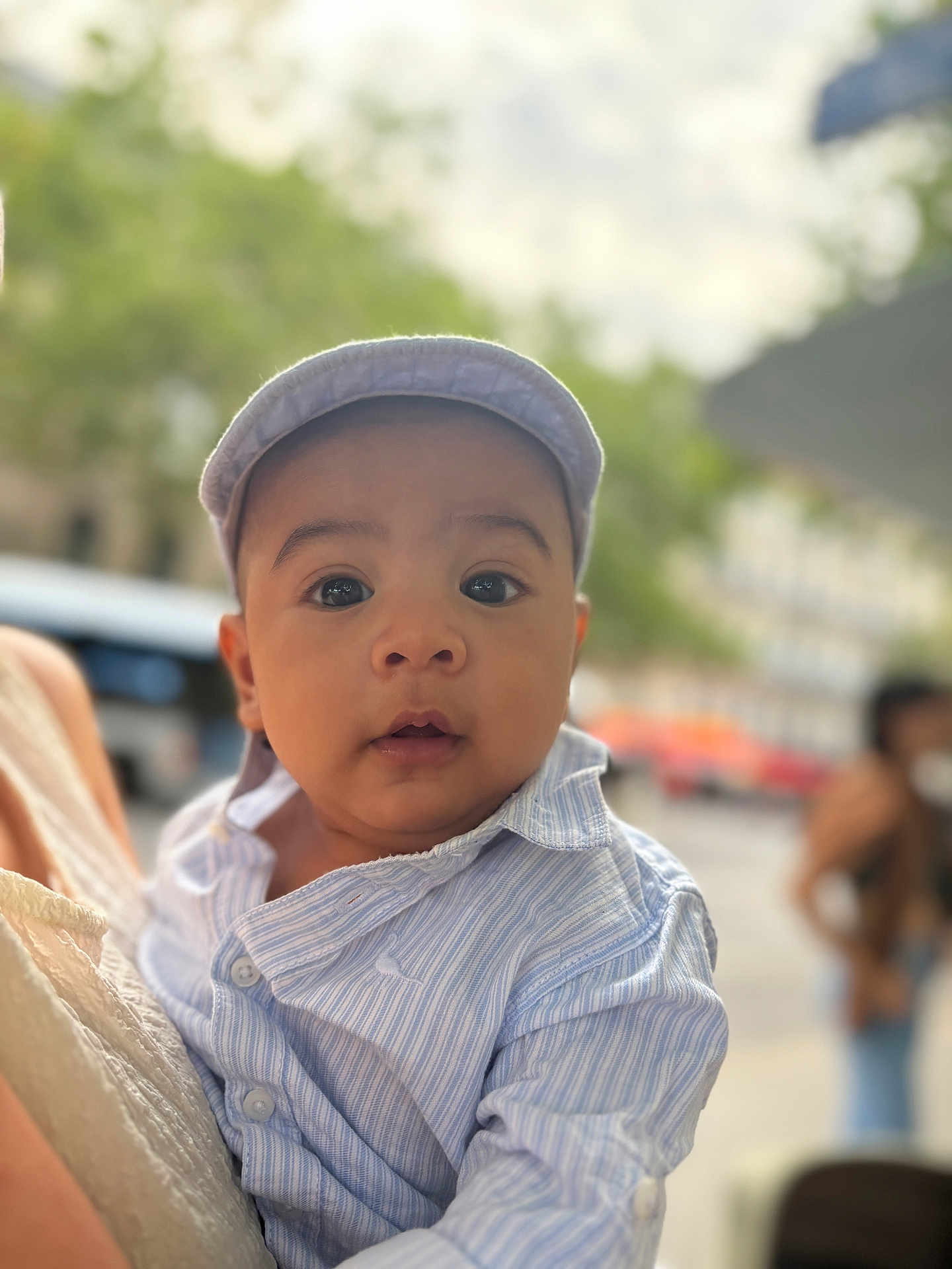 Antoine participe au concours pour gagner de l'argent avec cette photo : baby, child, infant, face, hat, cap, shirt, striped_shirt, person, outdoor, urban, blurred_background, curious, portrait, close_up, holding, adult, daylight, expression, cute
