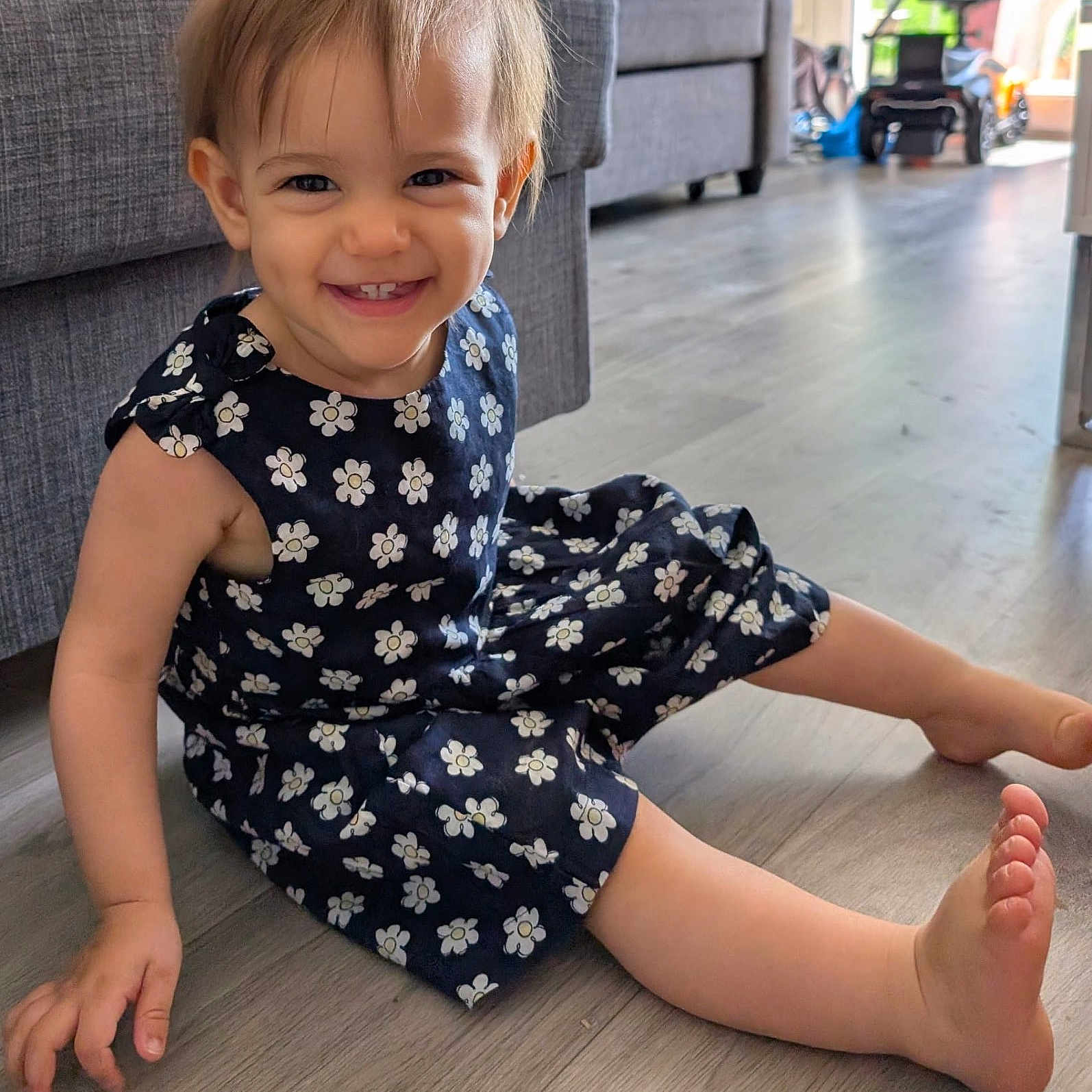 Soleya a rejoint le concours — aidez-le/la à gagner de superbes lots ! barefoot, casual, child, couch, cute, dress, floor, flower_pattern, furniture, happy, home, indoor, living_room, person, portrait, sitting, smiling, toddler, wooden_floor, young_child