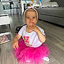 Soleya participe au concours pour gagner de l'argent avec cette photo : baby, toddler, child, pink_tutu, headband, smiling, indoor, wooden_floor, couch, pillow, toy, table, chair, birthday_shirt, person, cute, happy, living_room, floor, playful