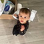 Soleya participe au concours pour gagner de l'argent avec cette photo : toddler, child, baby, floor, cardboard_box, paper_towel, curious, looking_up, black_clothing, stars_pattern, indoor, wooden_floor, household_items, playful, cute, small_hands, young_child, casual, expression, person