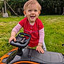 toddler, child, smiling, toy_car, outdoor, grass, red_shirt, play, happy, steering_wheel, greenery, nature, person, young_child, vehicle, cute, fun, daylight, casual_clothing, lawn