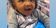 Kenzo is registered to the contest to win money with this photo: baby, child, hoodie, blanket, smiling, indoor, shopping_aisle, sitting, person, face, cute, happy, clothing, earrings, headwear, blue, gray, store, retail, emojis