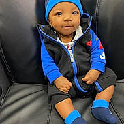 Kenzo is registered to the contest to win money with this photo: baby, child, nike, blue_beanie, blue_socks, black_leather_couch, casual_clothing, cute, indoor, infant, jacket, smiling, sitting, young_child, portrait, fashion, comfortable, clothing, person, headwear