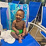 Kenzo is registered to the contest to win money with this photo: baby, child, smiling, blue_chair, green_shorts, towel, indoor_pool, plant, window, laughing, bare_chest, seat, furniture, happy, person, young_child, cute, playful, skin, relaxing
