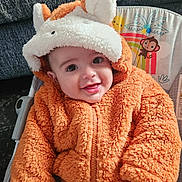 Cole is registered to the contest to win money with this photo: baby, child, orange_jacket, hood, ears, smile, happy, infant, cute, plush, seated, baby_seat, illustration, monkey, sun, clothing, portrait, face, warm, cozy