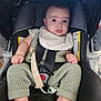 baby, car_seat, pacifier, knitwear, infant, child, seatbelt, straps, clothing, foot, hand, face, person, indoors, sitting, expression, cute, comfort, safety, bibs
