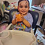 toddler, child, smiling, high_chair, toy, indoor, curly_hair, baby, happy, person, furniture, play, room, clothing, seat, table, face, hand, expression, home