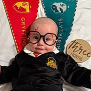 Yasin is registered to the contest to win money with this photo: baby, infant, glasses, wizard_costume, harry_potter, scar, gryffindor, slytherin, banner, blanket, wooden_sign, three_months, cute, portrait, lying_down, child, costume, black_clothing, white_collar, indoor