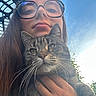 animal, cat, closeup, daylight, expression, face, feline, glasses, greenery, hand, holding, long_hair, nature, outdoor, person, pet, portrait, sky, tabby_cat, young_adult