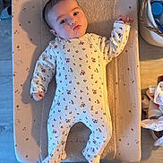 Romane participe au concours pour gagner de l'argent avec cette photo : baby, infant, onesie, floral_pattern, changing_pad, shadow, face, hand, footed_pajamas, indoor, wooden_floor, basket, household_items, soft_texture, calm, lying_down, person, cute, child, newborn