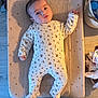 baby, infant, onesie, floral_pattern, changing_pad, shadow, face, hand, footed_pajamas, indoor, wooden_floor, basket, household_items, soft_texture, calm, lying_down, person, cute, child, newborn