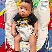 Grayson is registered to the contest to win money with this photo: baby, infant, child, bouncer, lion_king, clothing, onesie, face, legs, hands, socks, playmat, colorful, toy, animal_print, indoor, cute, portrait, seat, expression