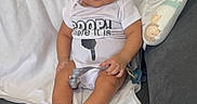 Grayson is registered to the contest to win money with this photo: baby, child, infant, couch, blanket, onesie, socks, remote_control, indoor, furniture, person, seated, curious_expression, hair, skin, face, hand, foot, white, gray