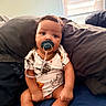 Grayson is registered to the contest to win money with this photo: baby, pacifier, onesie, dinosaur_pattern, socks, pillow, bed, window, blinds, indoor, child, cute, sitting, infant, natural_light, skin, face, hair, expression, clothing