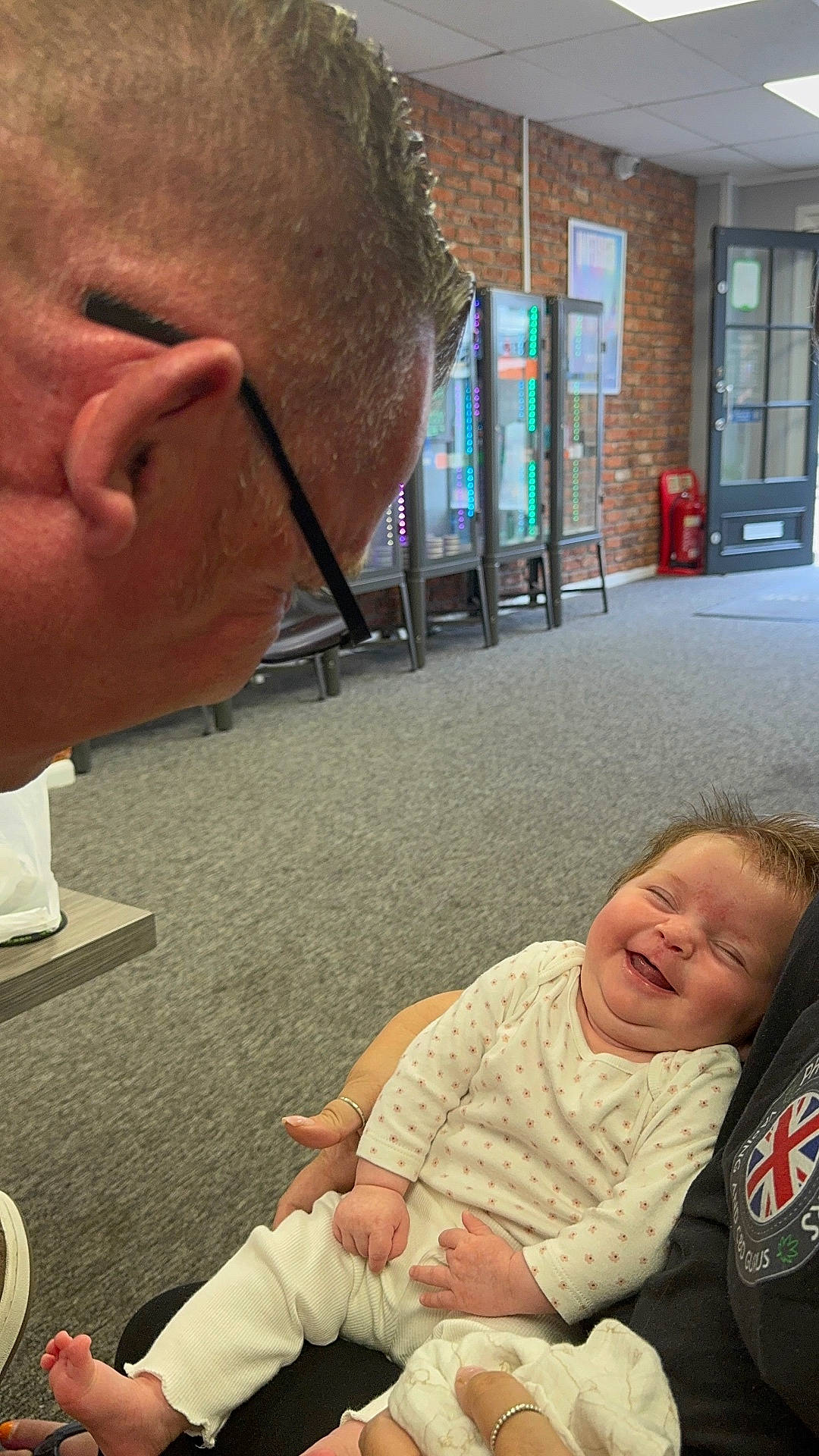 Evelyn joined the competition — help win amazing prizes! baby, brick_wall, carpet, clothing, family, glasses, hand, happy, head, holding, indoor, infant, interaction, laughing, man, person, portrait, sitting, smiling, vending_machine