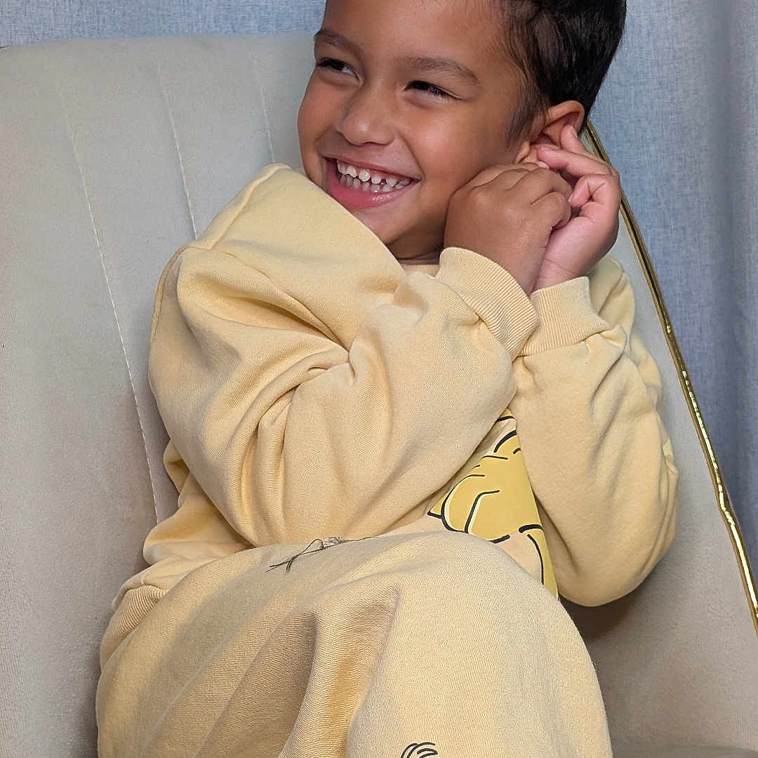 Oviyan participe au concours pour gagner de l'argent avec cette photo : beige_chair, cartoon_print, child, clothing, cozy, cute, face, fun, happy, indoor, light_background, person, playful, portrait, relaxed, short_hair, sitting, smiling, yellow_pajamas, young_child