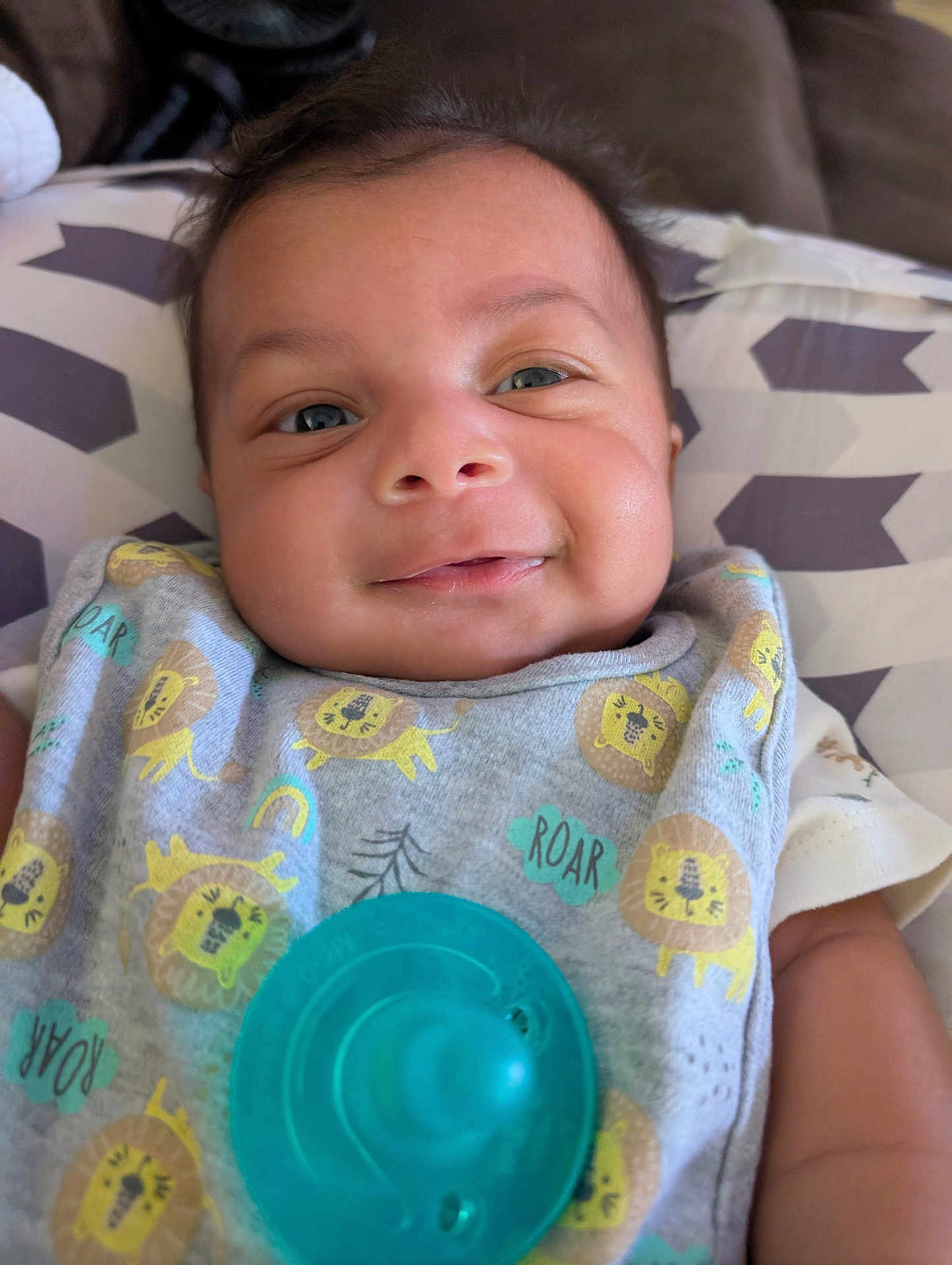 Sebastian joined the competition — help win amazing prizes! baby, smiling, face, infant, pacifier, bib, clothing, pattern, lion_print, cushion, closeup, person, child, happy, cute, indoors, young, skin, head, background