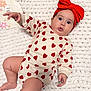 baby, infant, onesie, heart_pattern, red_headband, bow, knit_blanket, milestone_board, surprised_expression, chubby_cheeks, blue_eyes, lying_down, hand, foot, portrait, indoor, soft_lighting, cozy, skin_tone, newborn