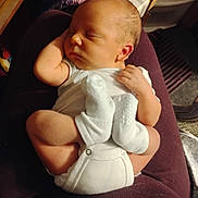 Rylan is registered to the contest to win money with this photo: baby, newborn, sleeping, infant, onesie, socks, curled_up, peaceful, resting, human, child, small, cute, soft_lighting, indoors, closeup, skin, head, face, hand
