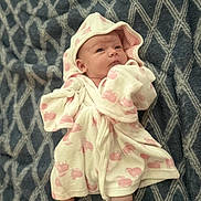 Sophia is registered to the contest to win money with this photo: baby, infant, robe, blanket, pattern, pink, white, clothing, sleepwear, foot, face, head, cute, newborn, lying_down, soft, cozy, indoor, child, portrait