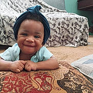 Reshard joined the competition — help win amazing prizes! baby, smiling, head_wrap, cushion, blanket, couch, carpet, indoor, child, happy, person, patterned, cozy, living_room, portrait, infant, face, hands, clothing, home