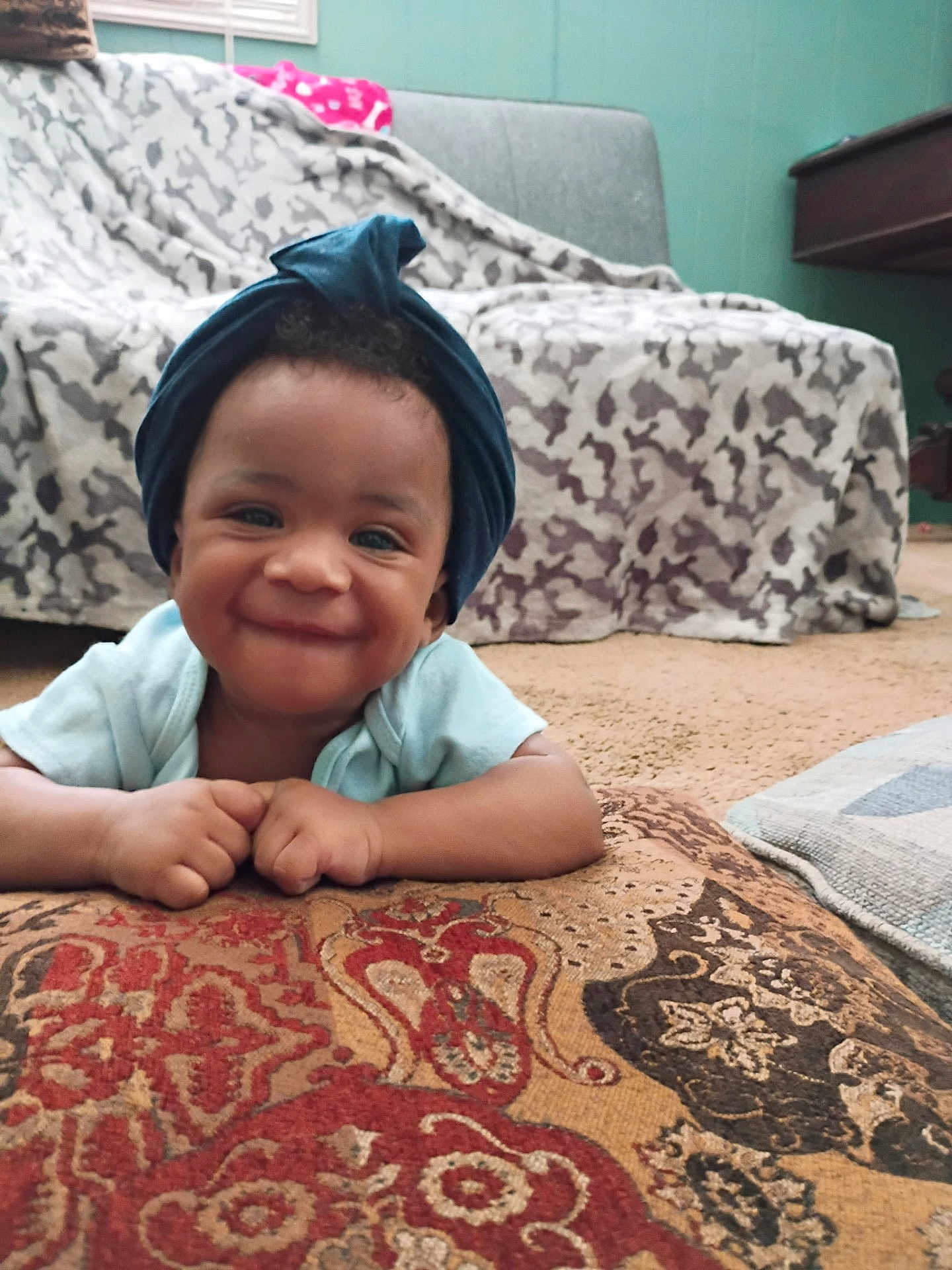 Reshard joined the competition — help win amazing prizes! baby, smiling, head_wrap, cushion, blanket, couch, carpet, indoor, child, happy, person, patterned, cozy, living_room, portrait, infant, face, hands, clothing, home