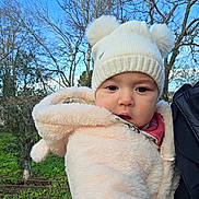 Anaya participe au concours pour gagner de l'argent avec cette photo : baby, child, winter_clothing, hat, pom_poms, jacket, outdoor, trees, sky, person, face, cute, cold_weather, nature, greenery, portrait, expression, infant, holding, warm_clothes