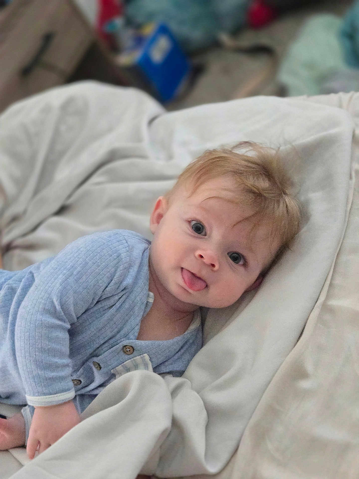 Christian joined the competition — help win amazing prizes! baby, tongue_out, blue_clothing, blanket, soft_texture, indoor, child, cute, infant, face, person, lying_down, bedroom, comfort, happy, young_child, long_sleeves, pale_skin, hair, expression