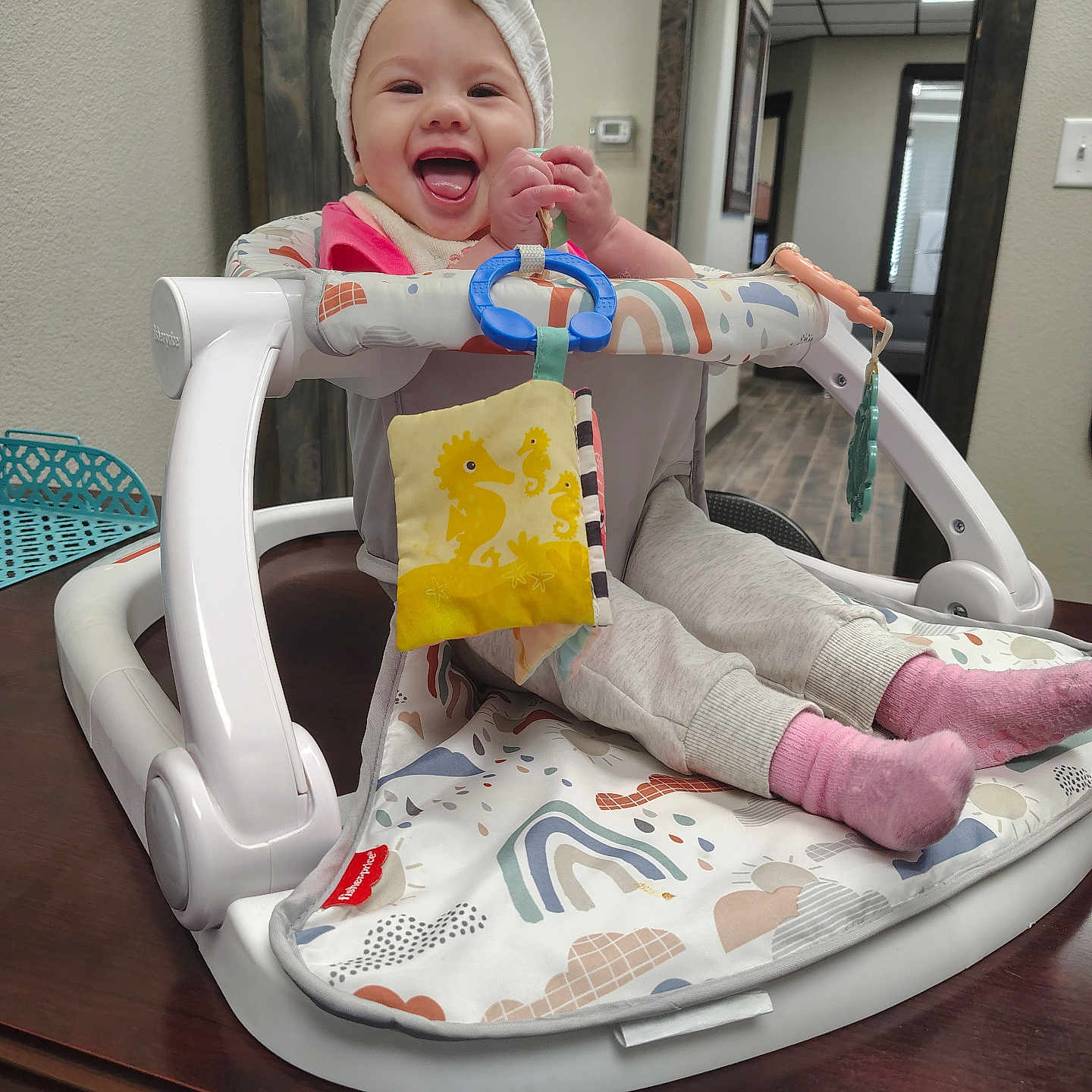 Jamie Lynn joined the competition — help win amazing prizes! baby, child, colorful, cute, face, furniture, happy, headwear, home, indoor, pants, person, pink_socks, playtime, seated, smiling, table, towel, toy, walker