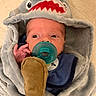 Bryer is registered to the contest to win money with this photo: baby, infant, pacifier, plush_toy, blanket, hood, shark_design, blue_clothing, soft_texture, cute, child, newborn, wrapped, indoor, portrait, small_hand, expression, cozy, looking_away, adorable