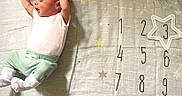 Bryer is registered to the contest to win money with this photo: baby, infant, milestone_blanket, numbers, planets, stars, stretching, white_onesie, green_pants, white_socks, cute, sleepy, newborn, soft_lighting, fabric, pattern, milestone_marker, child, indoors, portrait