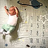 baby, infant, milestone_blanket, numbers, planets, stars, stretching, white_onesie, green_pants, white_socks, cute, sleepy, newborn, soft_lighting, fabric, pattern, milestone_marker, child, indoors, portrait