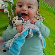 Aylan participe au concours pour gagner de l'argent avec cette photo : baby, child, smiling, toy, blanket, pajamas, cartoon_characters, play_mat, green, wooden_floor, happy, infant, cute, holding, lying_down, indoors, clothing, face, person, soft_toy