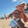 Marley joined the competition — help win amazing prizes! baby, child, beach, sunhat, smile, person, ocean, sand, summer, sunny, blue_sky, clouds, tropical, swim_shorts, happy, holding, wristwatch, bracelet, vacation, outdoor