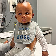 Marley joined the competition — help win amazing prizes! baby, infant, child, bib, mister_little_boss, tattooed_hands, clothing, white_long_sleeve, gray_pants, indoor, medical_office, table, curious_expression, person_holding_baby, face, skin, head, portrait, sitting, furniture