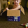 toddler, child, cardboard_box, indoor, carpet, toy, diaper, curious, looking_up, floor, brown, door, plastic_toy, container, young_child, playtime, room, casual, home, person