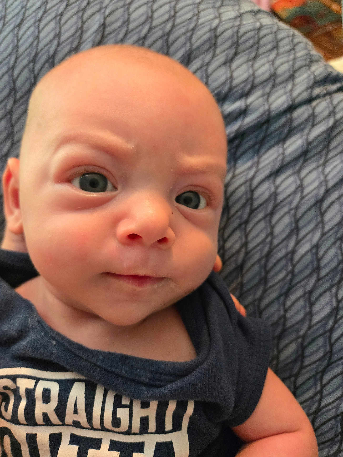 Christopher joined the competition — help win amazing prizes! baby, infant, face, eyes, expression, clothing, blue_shirt, blanket, closeup, portrait, skin, head, person, young_child, indoor, curious, sitting, small_person, human, cute
