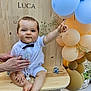baby, child, bow_tie, white_shirt, shorts, balloons, wooden_bench, hand, flowers, celebration, pointing, face, legs, feet, outdoor, party, decorations, pacifier_chain, smile, person