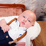 Thibault participe au concours pour gagner de l'argent avec cette photo : baby, infant, blue_eyes, white_shirt, suspenders, blanket, vintage_suitcase, wooden_table, flower_vase, indoor, portrait, cute, chubby_cheeks, lying_down, soft_texture, casual_clothing, skin, head, hand, relaxation