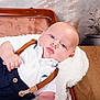 baby, infant, blue_eyes, white_shirt, suspenders, blanket, vintage_suitcase, wooden_table, flower_vase, indoor, portrait, cute, chubby_cheeks, lying_down, soft_texture, casual_clothing, skin, head, hand, relaxation