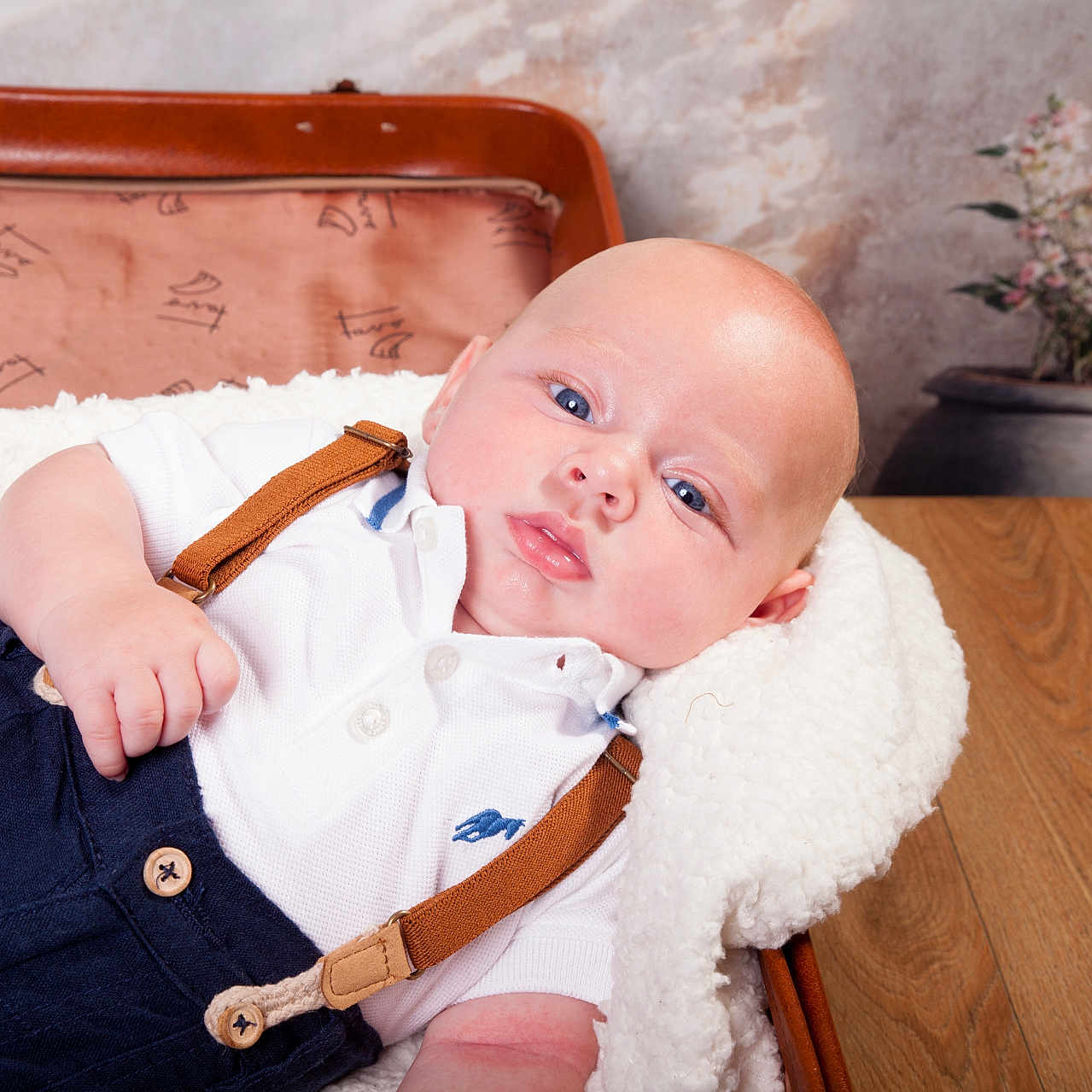 Thibault participe au concours pour gagner de l'argent avec cette photo : baby, blanket, blue_eyes, casual_clothing, chubby_cheeks, cute, flower_vase, hand, head, indoor, infant, lying_down, portrait, relaxation, skin, soft_texture, suspenders, vintage_suitcase, white_shirt, wooden_table
