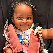 Azelia is registered to the contest to win money with this photo: baby, child, smiling, curly_hair, car_seat, safety_harness, toy, pink_beads, daisy_duck, clothing, cute, portrait, infant, happy, indoors, person, closeup, expression, seat, accessory