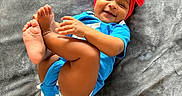 Azelia is registered to the contest to win money with this photo: baby, child, smiling, blue_onesie, red_bow, headband, feet, hands, blanket, soft_texture, happy, cute, infant, playful, lying_down, indoors, portrait, one_person, toddler, skin