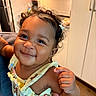 Azelia joined the competition — help win amazing prizes! baby, child, smiling, curly_hair, hair_clip, drool, colorful_clothing, cartoon_print, kitchen, cabinet, hand, skin, person, indoors, happy, cute, infant, portrait, holding, furniture