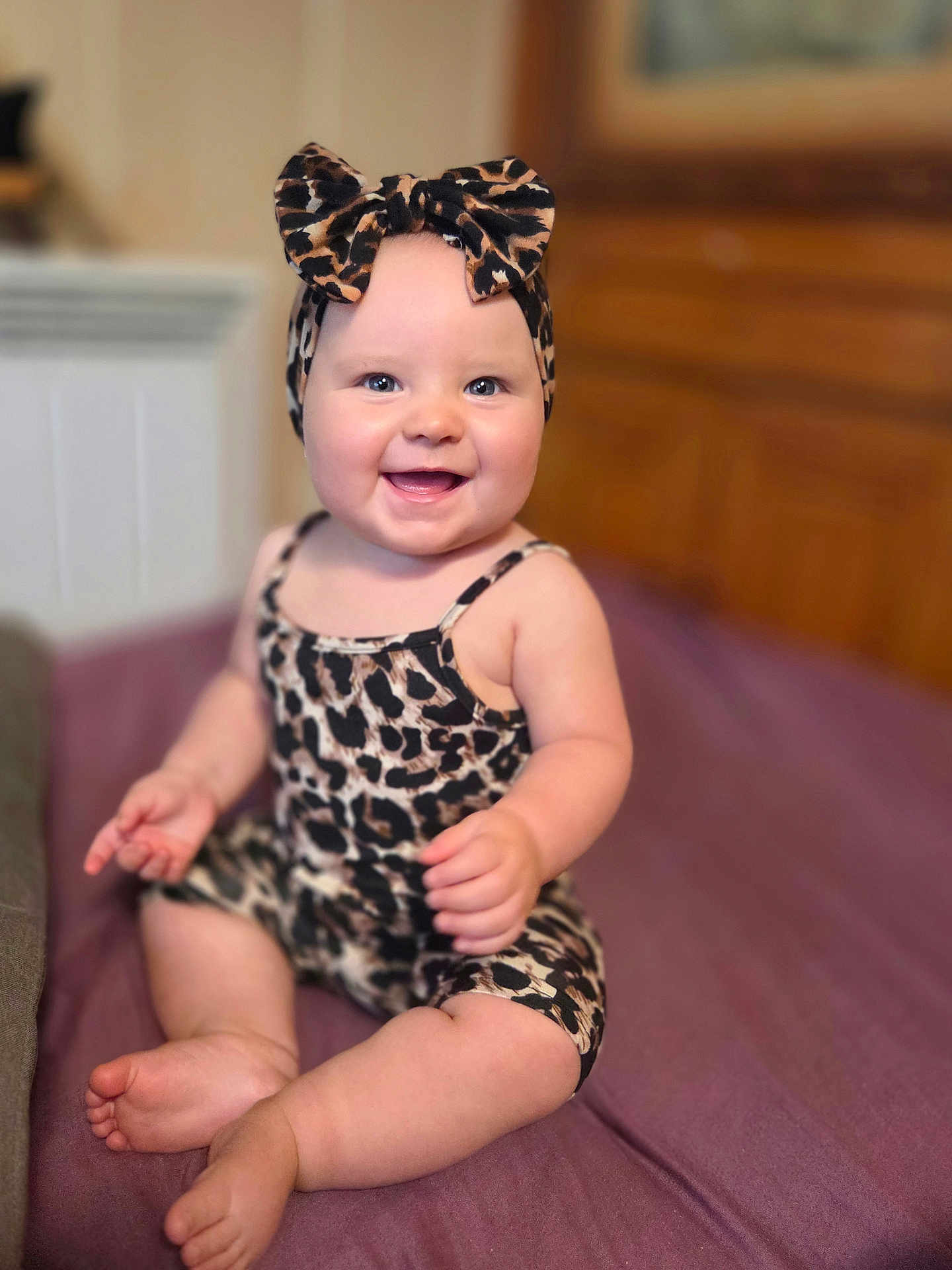 Nina a rejoint le concours — aidez-le/la à gagner de superbes lots ! baby, infant, smiling, sitting, leopard_print, headband, bow, clothing, indoor, portrait, child, happy, furniture, purple_bedspread, skin, cute, young_child, person, face, feet