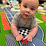 baby, infant, child, toy_car, play_mat, racetrack, carpet, crawling, hands, closeup, portrait, big_eyes, cute, indoor, soft_lighting, bokeh, foreground, colorful, checkerboard, onesie