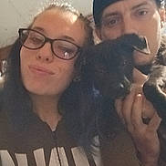 Arrow is registered to the contest to win money with this photo: beanie, black_dog, bond, casual, closeup, clothing, dog, face, friendship, glasses, happy, hat, holding, indoor, long_hair, person, portrait, selfie, smile, young_adult