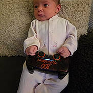 Charlie participe au concours pour gagner de l'argent avec cette photo : baby, infant, child, game_controller, gaming_controller, controller, onesie, clothing, hands, face, sitting, couch, cushion, blanket, indoor, portrait, cozy, curious_expression, small_hands, play